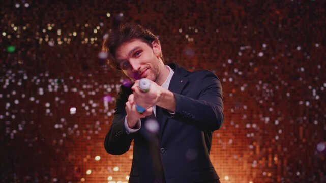 Attractive young man in suit blows up a popper at a party, having fun. Handsome male explosion a firecracker in his hands. Celebrating or holiday confetti. Victory at festival, congratulations.