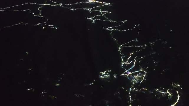 High angle nighttime drone footage capturing the massive scale of religious tourism in South Asia, featuring glowing Himalayan infrastructure from Katra city to the Vaishno Devi temple complex.