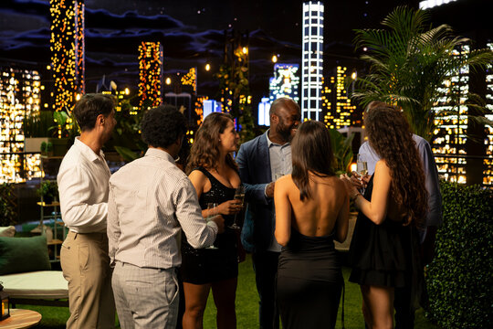 Friends mingle and socialize at a glamorous rooftop cocktail party, enjoying conversation and a luxury nighttime gathering on an urban terrace.
