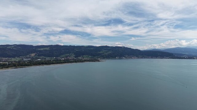 Aerial panoramic view of the eastern shore of Lake Constance near Bregenz, Austria, showing shallow turquoise water, exposed sandbanks, green wetlands, lakeside settlements and forested hills beneath 