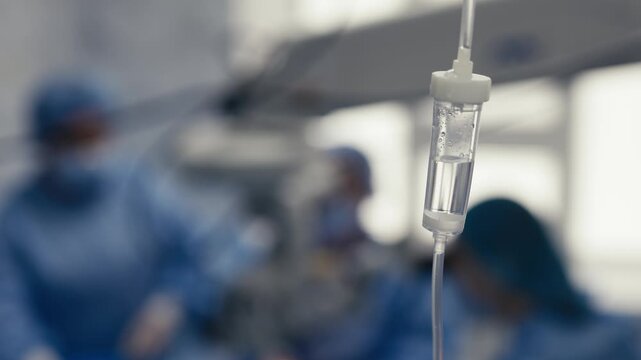 Intravenous drip chamber containing fluid in a hospital operating room. Medical infusion equipment during surgery.