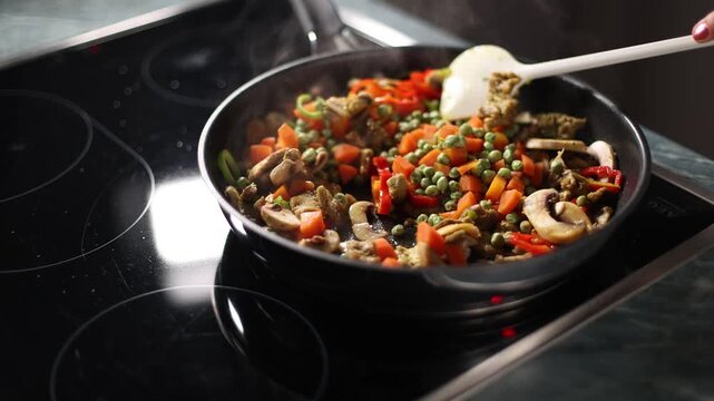 Vegetables are stirred into a pan with a wooden spoon
