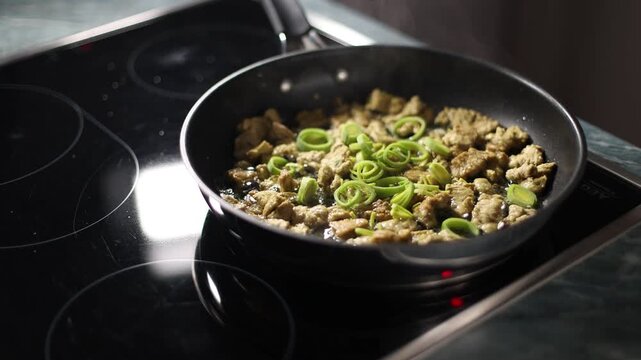 Leeks fall into a pan with fried pieces of soy