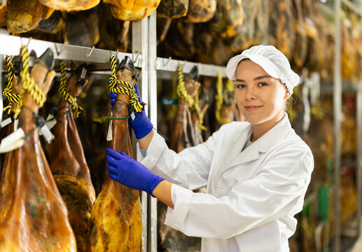 Girl employee checks jamon. Quality control, troubleshooting, search and elimination of violations. Meat processing plant. Hanging meat in production hall.