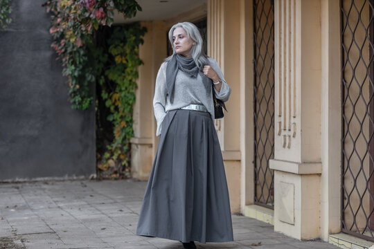 Elegant middle-aged woman in stylish gray outfit standing outdoors in city