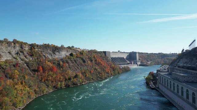 Aerial over the Niagara River between New York, United States and Ontario, Canada towards Niagara Falls Power Generating plant, hydroelectrical power plants. Autumn fall foliage trees, 2024.