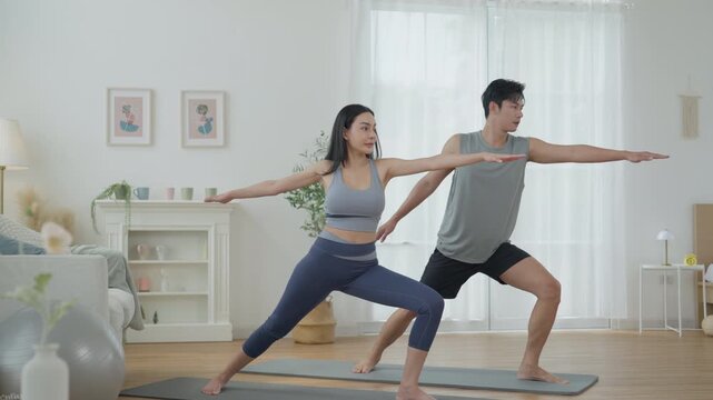 Asian couple practicing yoga and stretching exercise at home, building balance, fitness, family wellness, calm focus, supportive relationship, healthy lifestyle, and shared daily routine