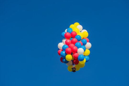 Cluster of colorful balloons lifting a small basket against blue sky