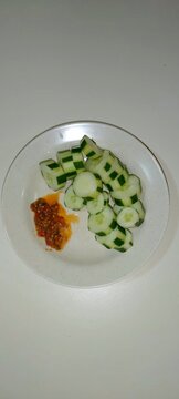 `Sliced cucumber with decorative cut and spicy sambal belacan chili shrimp paste on white plate, Malaysian healthy snack`