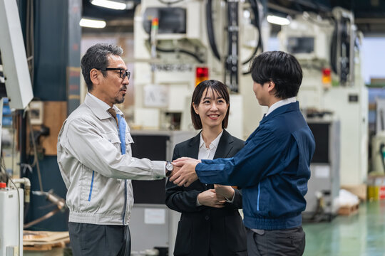 工場で握手する作業員グループ。事業承継、M&A、協力、チームワーク、仲介、紹介、コンサル、笑顔、契約