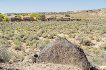 Petroglyph on volcanic boulder in desert landscape near suburban homes © Kit Leong