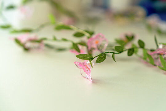 A trailing vine of pink translucent plastic blossoms and green fabric leaves rests on a pale tabletop indoors, a concept of romantic spring styling.