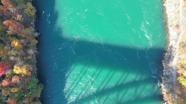 Aerial looking down over turquoise Niagara River, shadow of border crossing Queenston-Lewiston bridge between New York and Ontario, Canada. Autumn foliage leaves and birds, October, 2024.