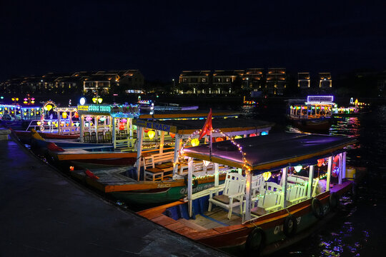 Traditional wooden passenger boats decorated with glowing lanterns are moored along the riverfront in Hoi An at night, Vietnam, Hoi An, July 7, 2026, central Vietnam.