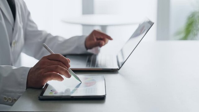 A man in a white coat working with a laptop and a tablet PC. Science, research, medicine, doctor, experiment, data, analysis.