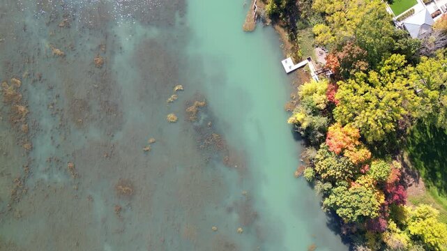 Aerial moving forward over Martindale Pond, looking down over the lakeside shoreline, in St. Catharines, Ontario, Canada on a sunny Autumn day in October, 2024.