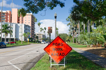 Bright orange road work sign in St. Petersburg, FL on a palm-lined city street beside condominiums, signaling maintenance and lane changes on a sunny day with clear skies and residential landscaping.  © Del Harper