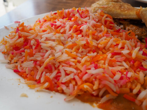 Traditional Somali Mandi Rice with Vibrant Orange and Yellow Food Coloring Accents served with Sabaayad Flatbread, Side Perspective View
