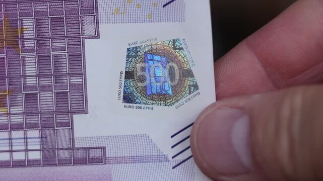 Close up video. Fingers holding edge of five hundred euro paper banknote with holographic foil patch security symbol. Cash money of European Union, EU. Pay tax, credit, debt, loan. 500 euro bill. Bank