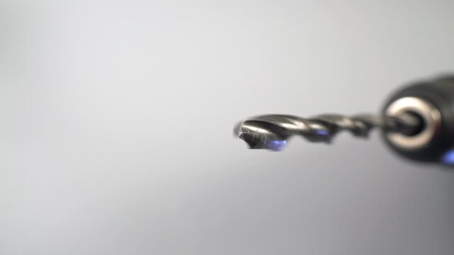 Extreme macro close up of a metal twist drill bit spinning in an electric drill chuck against a soft gray background, dolly shot of rotating steel