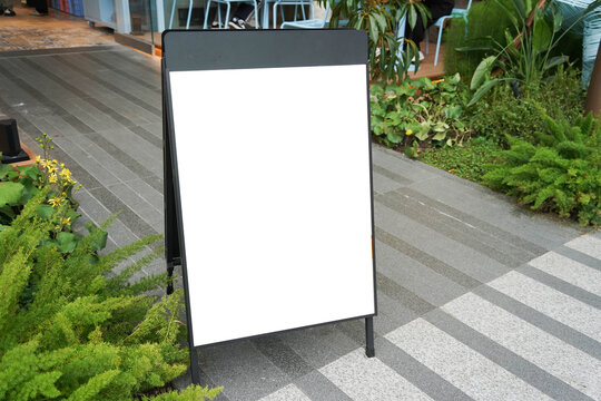 Blank white outdoor advertising stand sandwich board mock up template. Clear street signage board placed by an outdoor dinning area of a restaurant.