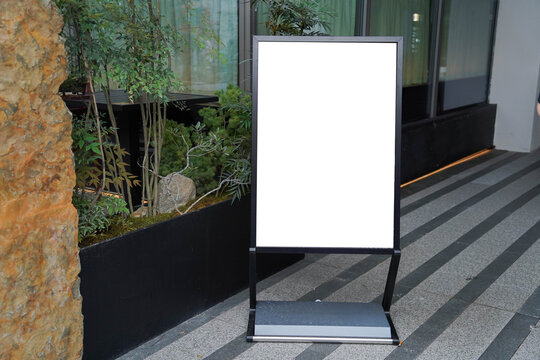 Blank white outdoor advertising stand sandwich board mock up template. Clear street signage board placed by an outdoor dinning area of a restaurant.