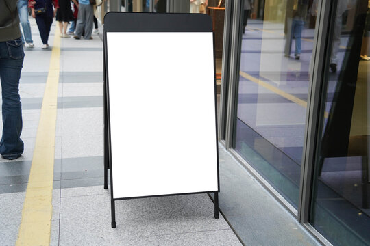 Blank white outdoor advertising stand sandwich board mock up template. Clear street signage board placed by an outdoor dinning area of a restaurant.