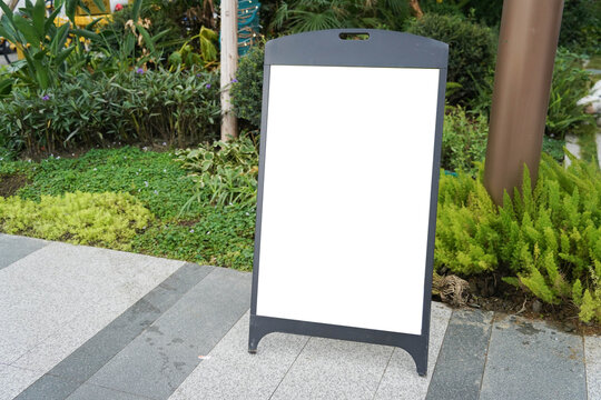 Blank white outdoor advertising stand sandwich board mock up template. Clear street signage board placed by an outdoor dinning area of a restaurant.