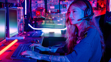 Woman hacker sitting in front of a computer typing on keyboard hacking servers in neon light, Female hacker breaks into data center, Gamer woman streaming game online © sorapop