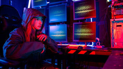 Woman hacker. A woman wearing a hood is thinking looking at a computer monitor. The room is dimly lit. possibly typing or browsing the internet, Hacker in neon light © sorapop