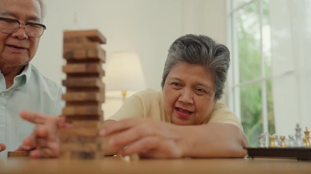 Senior woman senior man play block game with concentration at home indoor leisure in retirement couple family enjoying wooden tower activity together with calm support and companionship