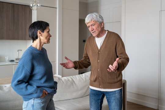 Stressed worried elderly husband arguing with unimpressed disappointed wife in living room, senior married couple communication breakdown and misunderstanding, nervous man talking to frustrated woman.