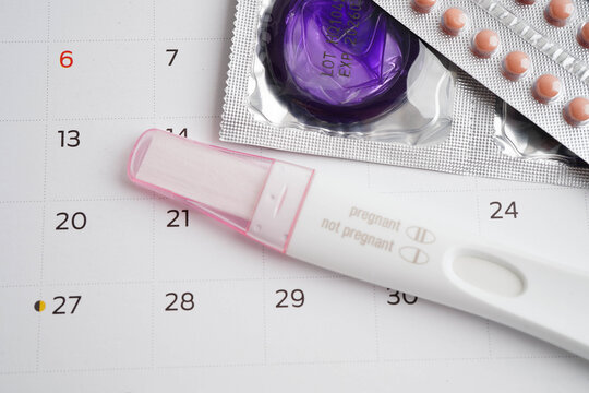 Pregnancy test with birth control pills and condom for female on calendar, ovulation day.