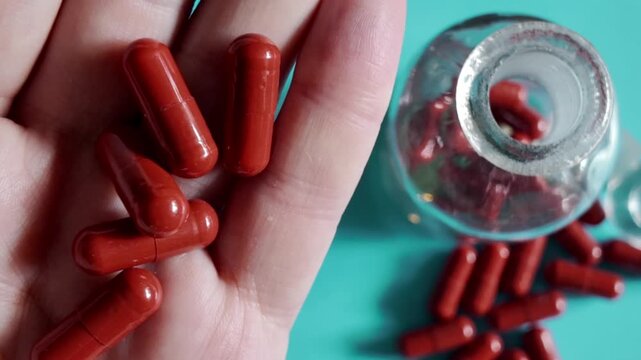 Close-up footage of a hand holding red capsules beside an open glass medicine bottle with selective focus.