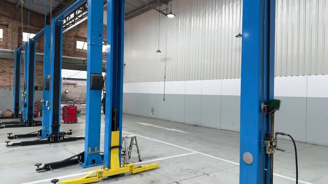 Modern auto repair workshop interior with multiple blue vehicle lifts standing idle in clean marked bays.