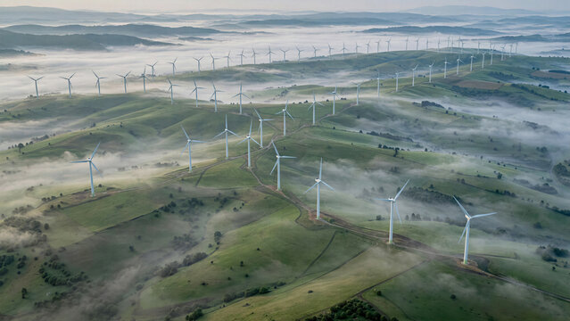 Cinematic drone shot of a massive onshore wind farm situated on rolling green hills during misty morning