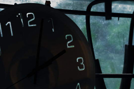 close-up view of a dark wall clock showing the time, framed against a window background