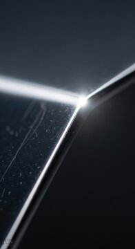 Macro photograph of a sharp polished metal corner reflecting bright light with lens flare, featuring surface texture scratches and dust on a dark black background.
