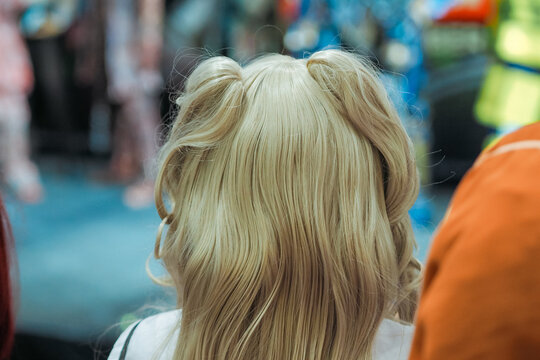 A back view close-up of a person wearing a blonde cosplay wig styled with double buns