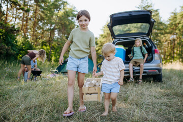 Naklejka premium Siblings unloading luggage from car and setting up a campsite.