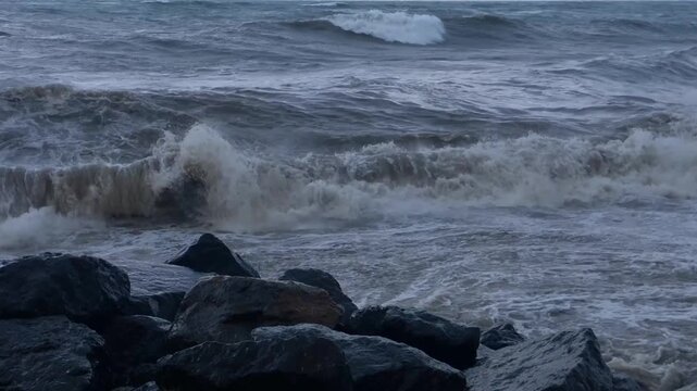 Close view of waves surging over shoreline boulders, with choppy Black Sea water foaming against dark rocks in Batumi, Georgia, for weather reports, coastal tourism and nature documentary use