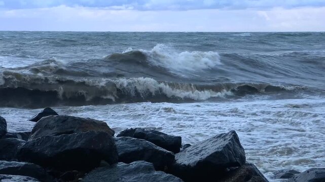 Low angle surf crashes against coastal rocks, showing rough Black Sea waves breaking along Batumi's pebble shore in Georgia for travel promotion, storm coverage and environmental storytelling