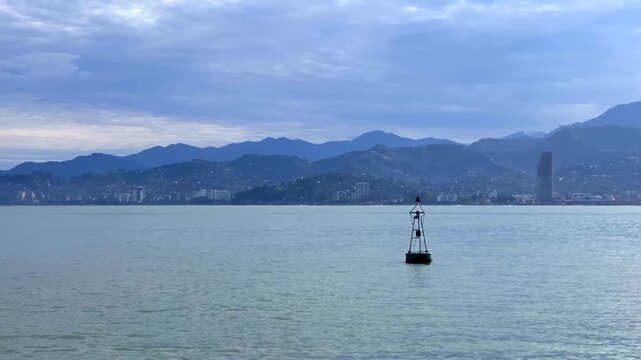 A channel marker floats offshore with Batumi and the Caucasus foothills behind it, providing context for nautical route planning, harbor approach guides and marine navigation materials for shipping