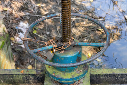 Close-up of a locked sluice gate valve wheel with chain and padlock. Water control mechanism on canal for agricultural irrigation system.