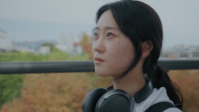 Close up portrait of a young woman with headphones around her neck looking away thoughtfully outdoors