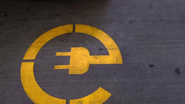 Yellow electric vehicle charging symbol is painted on asphalt, marking a designated parking bay for EV drivers and supporting wayfinding, parking management and transport electrification campaigns