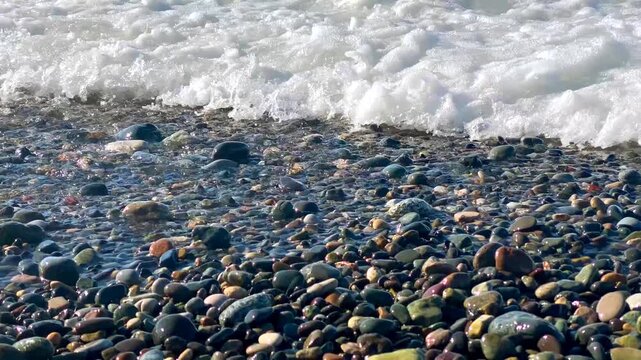 Close view of foaming surf breaks across smooth shoreline stones on Batumi coast, suitable for marine weather stories, coastal tourism campaigns, ocean movement footage and environmental reporting