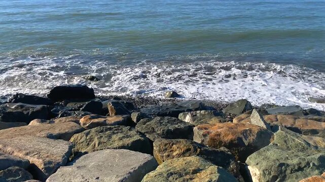 Small waves break against dark shoreline boulders on the Black Sea coast, creating a close study of coastal energy and natural textures suited to marine environment, weather and travel projects