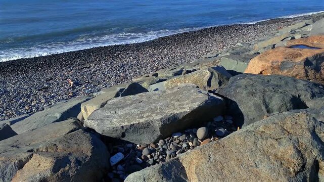 A pebble beach meets massive stone breakwater blocks as gentle surf rolls along Batumi Black Sea edge, illustrating shoreline protection and coastal infrastructure for environmental