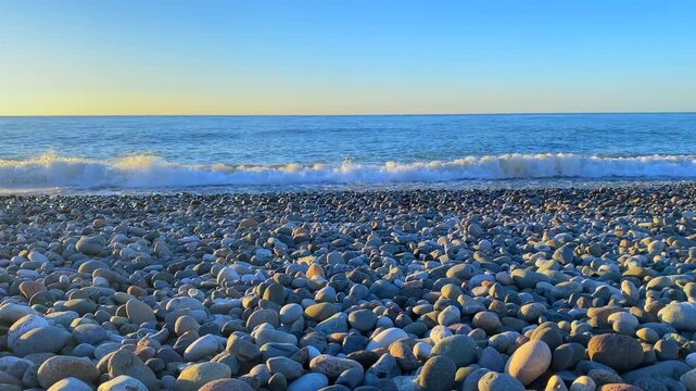 Small waves roll over a broad pebble beach beneath a pale evening sky. Empty Black Sea shoreline offers a clean setting for tourism, coastal weather reports and destination footage with open horizon